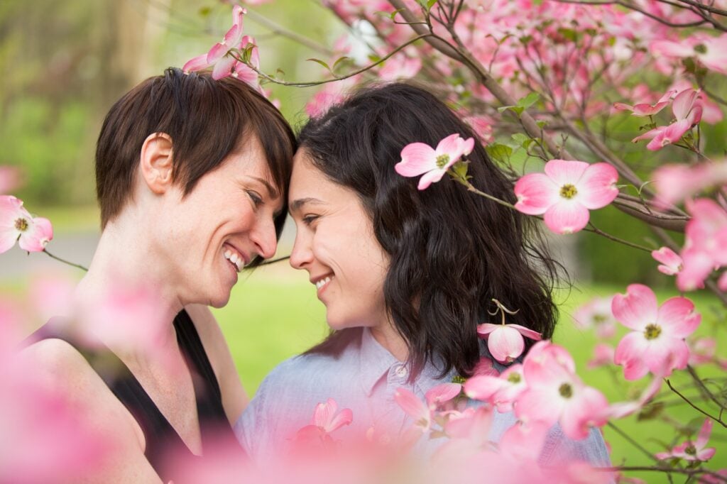 A same sex couple, two women under the branches of a flowering tree.